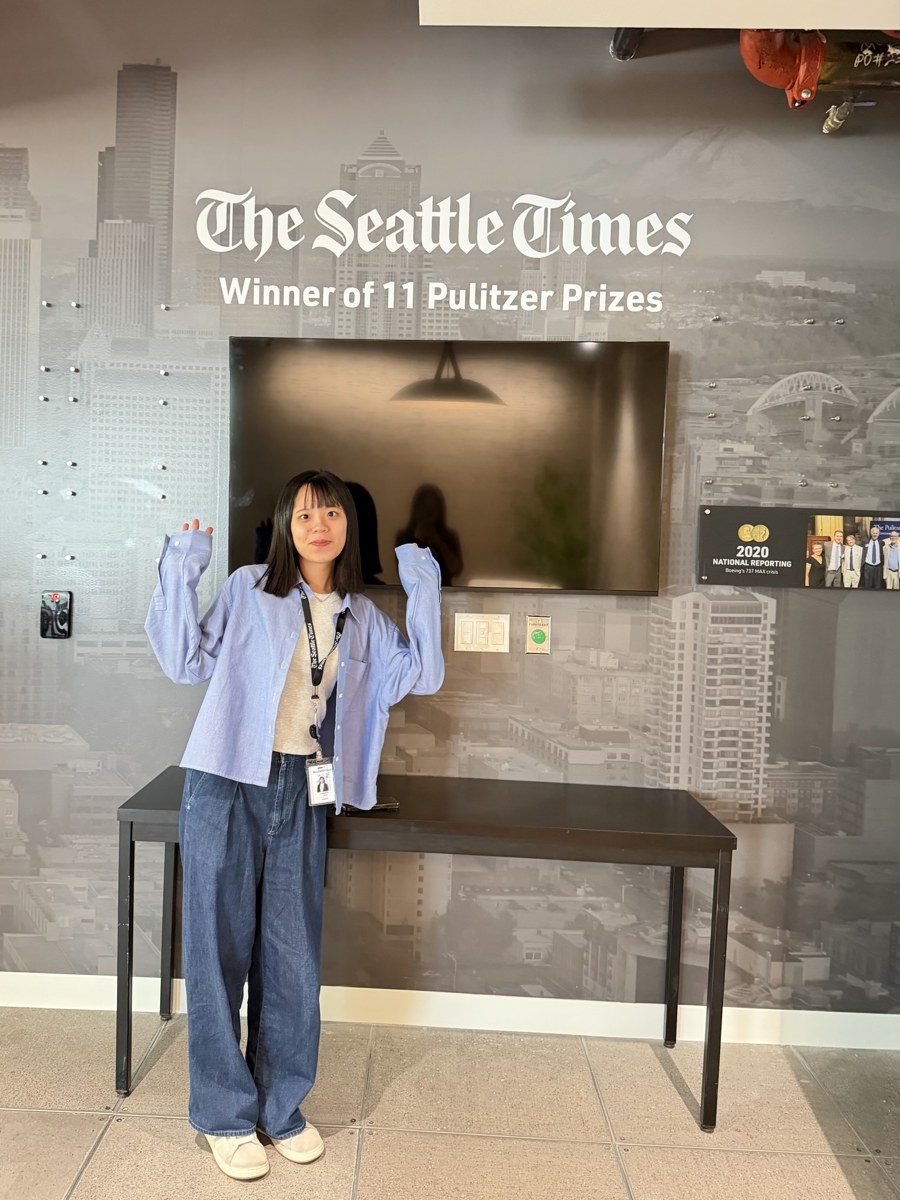 Winnie Yao standing in front of a Seattle Times office wall that reads 'The Seattle Times, Winner of 11 Pulitzer Prizes'